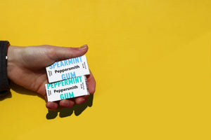 A hang holding Peppersmith Spearmint and Peppermint chewing gum on a yellow background