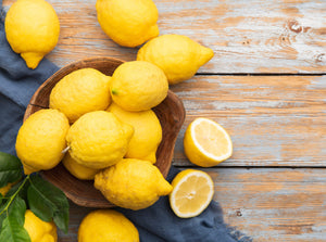 A bowl of lemons over flowing and slices next to it on a wooden table