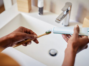 A wooden Tooth Brush with tooth paste being squeezed onto it